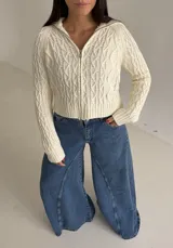Sweater tipo campera de tejido de punto con diseño de trenzas, color blanco, con cuello alto y cierre frontal completo.