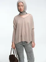 Sweater tipo poncho de cuello en V, confeccionado en tejido de punto suave. Presenta mangas largas con puños acanalados, corte holgado y aberturas laterales en el ruedo.