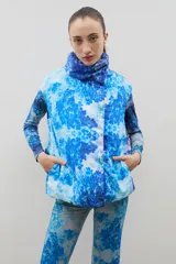 Chaleco puffer con cuello alto y cierre frontal oculto, con estampado forestal en tonos azules.
