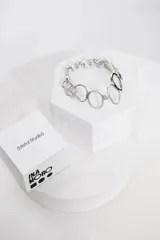 Pulsera de metal plateado de la marca Ina Moro, compuesta por una cadena de eslabones redondos combinada con dijes de aros ovalados entrelazados.