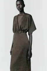 Vestido midi de tejido piqué en color marrón oscuro jaspeado, con escote en pico cruzado y mangas cortas. Presenta detalle de frunces en la cintura y un cinturón integrado con hebilla metálica a contraste.