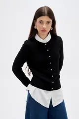 Saco de punto al cuerpo, color negro, con cuello redondo, manga larga y cierre frontal con botones pequeños.
