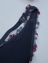 Pack de dos bralettes de encaje marca Jessica Simpson, con breteles fijos y espalda deportiva. Uno es de encaje floral color lila y el otro es de encaje floral multicolor sobre base azul.