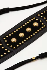 Cinturón tipo faja de cuero vacuno negro, con diseño ancho y decorado con tachas metálicas doradas. Incluye tiras largas con borlas en los extremos para anudar en la cintura.