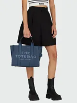 Bolso tipo tote de cuero azul, con diseño estructurado, doble asa superior y cierre superior con cremallera. Presenta el logo 'THE TOTE BAG MARC JACOBS' estampado en el frente.