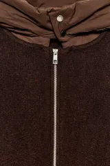 Chaqueta de punto color marrón con capucha desmontable en tejido técnico a tono. Presenta cierre frontal con cremallera, bolsillos delanteros y mangas largas con doble puño elástico.