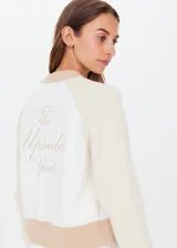 Bomber de punto color beige con mangas color crema, cuello, puños y ruedo acanalados en color marrón. Cierre frontal con botones a presión metálicos. Bordado "The Upside Sport" en la espalda.