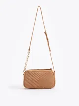 Bandolera de gamuza gris con diseño matelaseado en forma de V. Presenta un aplique metálico dorado en forma de labios en el frente y una correa combinada con cadena metálica dorada.