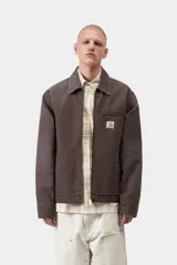 Chaqueta Detroit de Carhartt WIP color marrón, de corte recto con cierre frontal de cremallera, cuello clásico de pana y bolsillos laterales. Cuenta con un bolsillo con cierre en el pecho decorado con la etiqueta del logo de la marca.