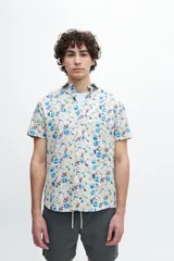 Camisa de manga corta con estampado floral en tonos celeste, azul y rojo. Tiene cuello clásico, calce regular, bolsillo en el pecho y botones personalizados.