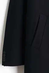 Abrigo de corte recto y largo hasta la rodilla, con solapas de muesca, cierre frontal de tres botones y bolsillos laterales insertados. Presenta un diseño clásico y estructurado con forro interior.