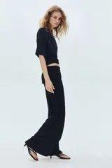 Pantalón negro de punto fino suave con piernas amplias y tiro alto. Presenta una cintura ancha con costuras laterales fruncidas para crear un efecto drapeado.
