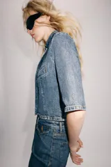 Blazer cropped de denim azul con cuello subido, manga corta y bolsillo de vivo en el pecho. Cierre frontal con botón.