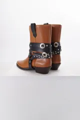 Bota de cuero color marrón con puntera fina y taco bajo. Presenta correas de cuero negro con apliques metálicos plateados.