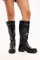 Bota de caña media en cuero sintético negro, con suela track, cierre lateral y detalle de tachas metálicas en la parte superior y en una tira decorativa sobre el tobillo.