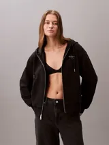 Buzo con capucha y cierre frontal de cremallera de la marca Calvin Klein, color negro, de corte regular cropped y manga larga. Presenta bolsillos tipo canguro, cordones ajustables en la capucha y el logo monograma de la marca estampado en el pecho.