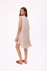 Vestido corto beige de lino, sin mangas, con escote redondo y detalle de abertura en forma de lágrima en el pecho. Presenta diseño holgado y dobladillo asimétrico más largo en la parte trasera con volados.
