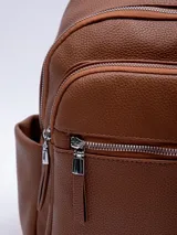 Mochila gris de símil cuero con textura granulada, asas regulables, cinco bolsillos externos con cierre y tres bolsillos internos.