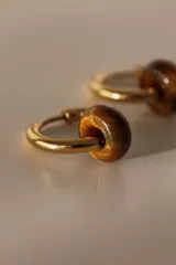 Par de aros tipo argolla dorados de acero quirúrgico, con una piedra natural de color gris translúcido colgando de cada uno.