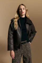 Campera tipo gamulán de cuero sintético negro, con interior y detalles de corderito sintético al tono en cuello y ruedo. Presenta cierre frontal metálico y diseño de silueta relajada.