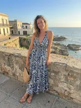 Vestido largo con estampado tribal en tonos azul índigo y blanco. Presenta un escote profundo en V con tirantes tipo halter y cintura elástica ancha que da paso a una falda con vuelo en capas.