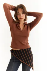 Top de manga larga color verde petróleo, con cuello polo y escote en V pronunciado. Presenta recortes diagonales en el frente y un pequeño bordado en el puño.