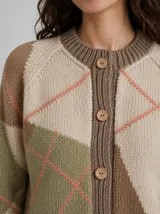 Cárdigan de punto con diseño geométrico de bloques de color en tonos tierra, verde y crema, con líneas finas en color coral. Presenta cierre frontal con botones, cuello redondo y mangas raglán.