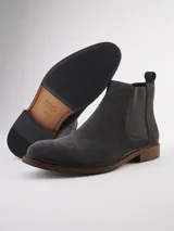 Bota Chelsea de gamuza gris con elásticos laterales, suela de goma marrón y tirador trasero.