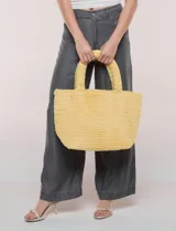 Cartera tipo shopper color amarillo de textura soft y flexible, con doble asa superior fija y compartimento principal amplio con botón metálico.