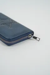 Billetera roja con diseño de estrella en el frente realizado con tachas metálicas oscuras. Cuenta con cierre de cremallera perimetral y tirador metálico.