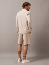 Camisa de manga larga color beige, corte slim, con cuello clásico, cierre frontal con botones, bolsillo de parche en el pecho y logo de Calvin Klein en el bolsillo.