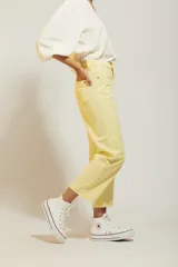 Pantalón de jean color amarillo pastel, de corte recto y tiro medio, con diseño de cinco bolsillos y cierre frontal con botón y cremallera.