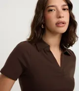 Blusa de cuello polo y manga corta, confeccionada en tejido rib de algodón con elastano. Presenta un diseño ajustado al cuerpo con escote en V y textura acanalada.