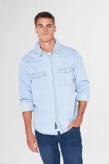 Camisa de jean celeste de manga larga, con cuello clásico, cierre frontal con botones a presión, dos bolsillos con solapa abotonada en el pecho, corte en hombros y detalle en la espalda.