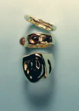 Set de tres anillos dorados de diseño irregular. Incluye un anillo ancho con forma orgánica, un anillo mediano incrustado con piedras marrones y un anillo fino con textura grabada.