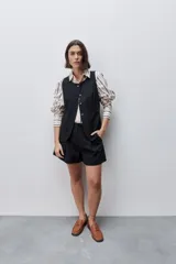 Short de tiro alto confeccionado en algodón, con calce relajado y silueta recta. Presenta pinzas delanteras, bolsillos laterales y botones decorativos en la cintura.