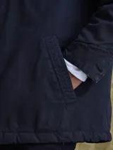 Campera de gabardina color azul marino, con cuello camisero, cierre frontal con botones metálicos y bolsillos frontales con solapa.