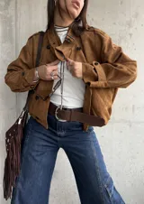 Campera tipo bomber de gamuza color camel, con diseño de doble botonadura frontal, cuello camisero y mangas largas con puños abotonados.
