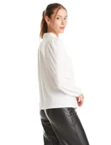 Blusa de seda fría color negro, con escote en V y lazo decorativo al cuello. Presenta mangas largas abullonadas con puños elásticos y detalles de strass aplicados en cuello, lazo y mangas.