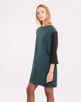 Vestido corto negro con mangas 3/4 verdes, cuello bote y bolsillos laterales.