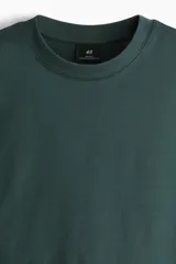 Remera verde oscuro de corte relajado, confeccionada en punto de algodón de peso medio, con cuello redondo ribeteado y hombros caídos.