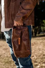 Necessaire de cuero natural marrón con diseño artesanal y funcional. Cuenta con laterales ajustables para adaptar su capacidad, interior forrado y reforzado, y cierre superior.