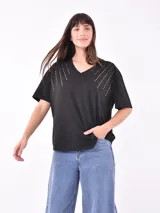Remera negra de manga corta con cuello en V y apliques de tachas doradas dispuestas en forma de abanico sobre los hombros.