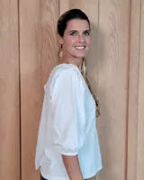 Blusa blanca de algodón tussor, con cuello redondo, mangas 3/4 abullonadas y detalle de volados en los hombros.