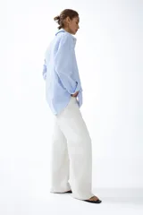 Camisa de corte relajado con diseño a rayas finas en tonos celeste y blanco, cuello clásico, mangas largas con puños anchos abotonados y bajo redondeado.