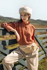 Camisa de algodón color marrón con cuello alto con volados, cierre frontal de botones y mangas largas con frunces en los hombros y puños abullonados.
