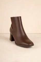 Botas de caña baja color negro, de símil cuero con punta redonda, cierre lateral, taco cuadrado y recorte en gamuza en la parte trasera.