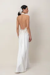 Vestido largo de seda natural color blanco, con escote halter tipo Marilyn y espalda descubierta. Presenta un elaborado bordado a mano con pedrería en la parte superior y caída fluida.