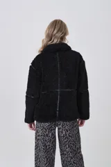 Campera de corderito color negro, con cuello alto y cierre frontal completo. Presenta detalles de vivos en cuero sintético en el cierre, bolsillos y costuras, además de una hebilla decorativa en el cuello.