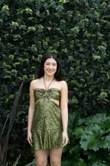 Vestido corto de lentejuelas color ciruela o morado oscuro, con escote corazón y detalle de argolla central que conecta con tirantes finos que atan al cuello. Presenta aberturas laterales (cut-outs) en la zona de la cintura y falda corta con vuelo.